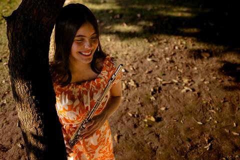 Garota com vestido de estampa laranja caminha com sua flauta  enquanto é fotografada no seu ensaio de aniversário por Mary Santtiago fotógrafa de Suzano SP'
