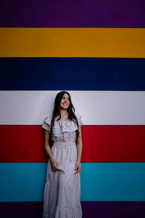 Garota sorridente com vestido poá, em frente a uma parede com listras coloridas e horizontais, foto de Mary Santtiago, fotógrafa de Suzano SP'