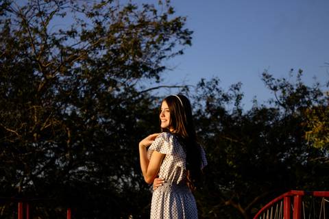 Garota de vestido branco e de costas, está coma mão no ombro e sorrido, enquanto posa para foto do seu ensaio de aniversário feito por Mary Santtiago, fotógrafa de Suzano  SP'
