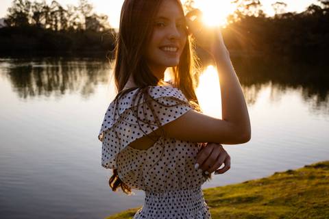 Garota de vestido de poá, posando para foto em frente a um lago durante o pôr-do-sol em seu aniversário de 13 anos, foto de Mary Santtiago fotógrafa de Suzano SP'