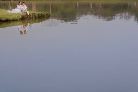 Casal sentado na beira de um lago conversando e descontraído'