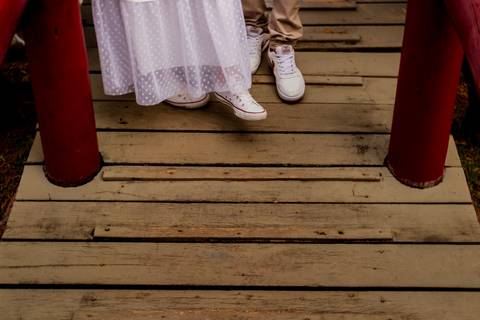 Foto dos pés do casal em uma ponte rústica de madeira'