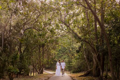 Casal caminhando em trilha por entre as árvores, enquanto são fotografados durante um ensaio pré-wedding'