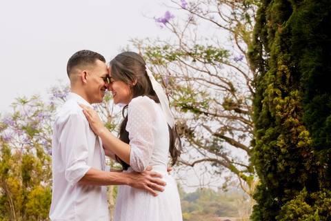 Casal abraçados posando para ensaio pré-wedding, com árvores ao fundo'