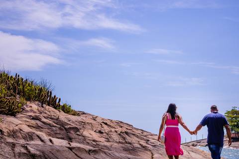 Casal caminhando em meio as pedras de mãos dadas. O clique foi capturado de uma forma que só aparecia uma beiradinha do mar. Foto feita por Mary Santtiago, fotógrafa de Suzano SP'