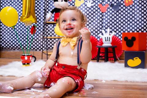 o bebê sorri com a cara cheia de cobertura do seu bolo Smash the Cake'