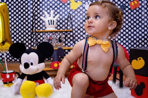fotografia do bebê tentado levantar no seu Smash the Cake com a decoração do Mickey Mouse, em um ensaio feito em casa'