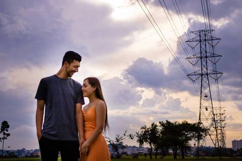 Nelly está segurando a mão de Matheus e posando para foto do Ensaio Pré-wedding, feito por Mary Santtiago, no Parque Max Feffer, o casal se encontra próximo a uma antena'
