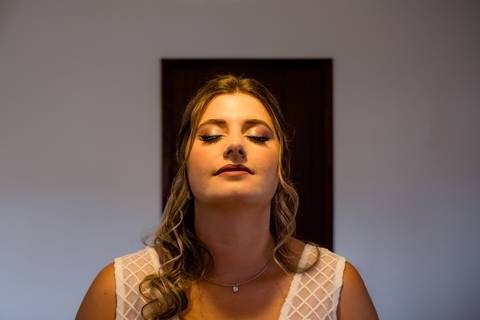 Uma mulher com olhos fechados e uma expressão calma. Ela tem cabelo longo e está usando uma blusa estampada sem mangas e um colar.'