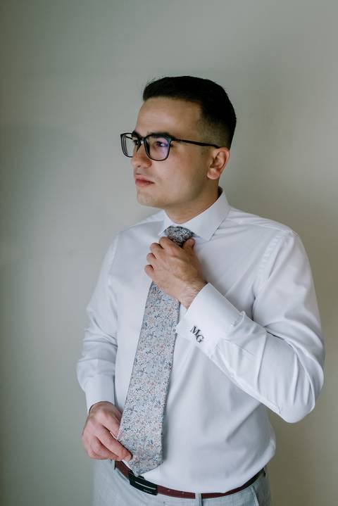 Noivo ajusta a gravata momentos antes do casamento, num registo elegante e confiante. Detalhe dos botões de punho personalizados adiciona um toque especial e sofisticado. Preparativos cheios de simbolismo e estilo.'