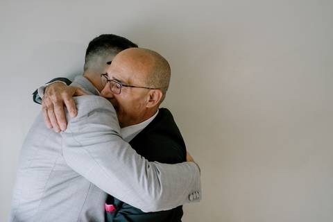 Um abraço emocionante entre o noivo e o pai, capturando um momento de ternura e afeto no dia do casamento. A expressão serena e sorridente revela a profundidade da ligação entre os dois. A fotografia transmite amor, gratidão e um vínculo inquebrável.'