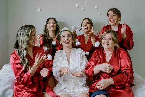 A preparação para o casamento é um momento especial, onde a noiva, usando um robe branco e uma teara, se destaca ao lado das damas.  Este cenário descontraído reflete a alegria do grande dia.'