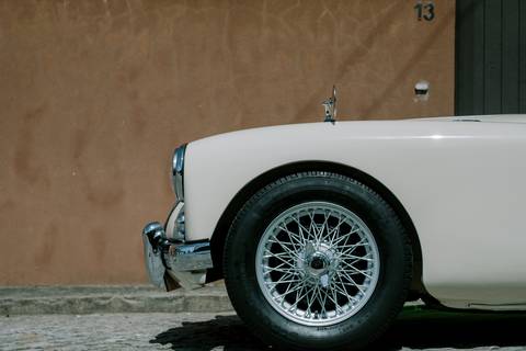 Carro clássico vintage branco, com rodas de raios metálicos, ideal para transportar noivos no dia do casamento. Elegância e estilo retrô que garantem charme e sofisticação para momentos únicos e fotografias inesquecíveis.'