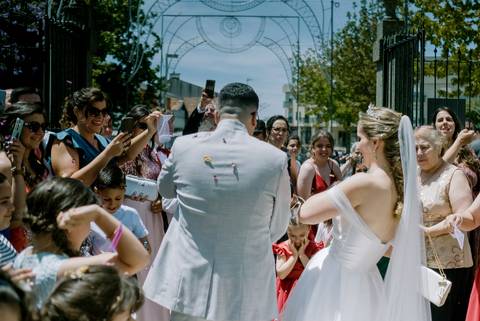 Casamento em Portugal com os noivos celebrando após a cerimónia religiosa, rodeados por convidados sorridentes a lançar pétalas. Destaque para a emoção e alegria do momento. casamento em Portugal, celebração, noivos felizes, cerimónia religiosa.'