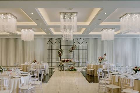 Espaço de casamento elegante com mesa dos noivos decorada com flores vermelhas e brancas, lustres de cristal imponentes. Salão ideal para eventos de luxo, oferecendo sofisticação e glamour. salão de casamentos, decoração floral, eventos de luxo'