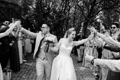Celebração de casamento vibrante captada em preto e branco, onde os noivos brindam com os convidados numa atmosfera de alegria e descontração. Ideal para destacar momentos únicos de união e felicidade. casamento alegre, fotografia de casamento.'