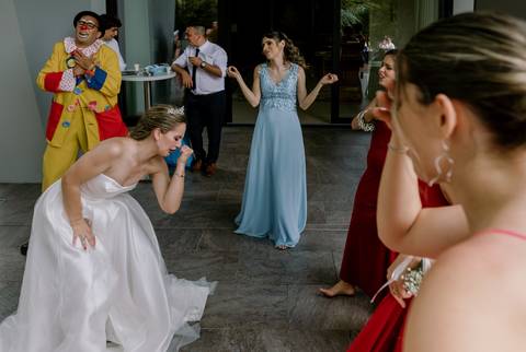 Momento divertido e animado no casamento, com a noiva a interagir com um palhaço, rodeada por  convidados sorridentes. Instantes únicos de celebração e alegria. diversão no casamento, noiva, damas de honra, celebração, fotografia de casamento '