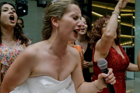 Noiva a cantar com entusiasmo durante a festa de casamento, rodeada por convidados animados. Momento de alegria e descontração captado no evento. noiva a cantar, festa de casamento, animação, celebração, momentos inesquecíveis, fotografia de casamento.'