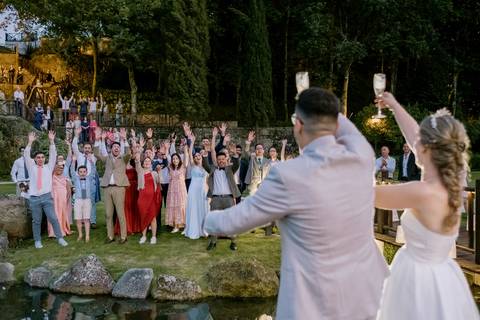 Noivos brindam com os convidados num casamento ao ar livre, com todos a celebrarem juntos num ambiente festivo e rodeado pela natureza. casamento, festa de casamento, brinde dos noivos, convidados, celebração, cerimónia ao ar livre.'