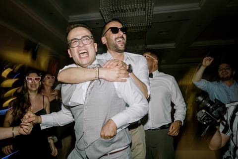 Momento de descontração e alegria durante a festa de casamento, com o noivo e amigos a rirem e celebrarem na pista de dança. Convidados animados e boa disposição captados num ambiente de festa. casamento, diversão, pista de dança, celebração, noivo.'