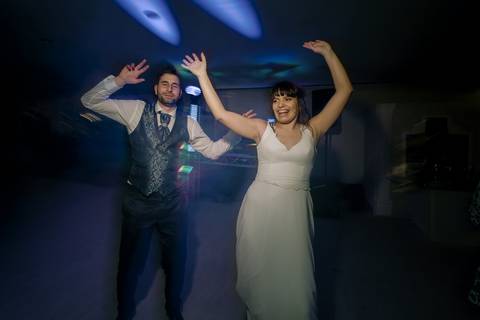 Noivos a dançar animados na pista de dança, com luzes coloridas a criar uma atmosfera festiva. Momento descontraído e cheio de alegria durante o casamento. Ideal para destacar a diversão e a celebração do grande dia. noivos, dança, casamento, festa.'