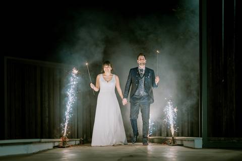 
Noivos a caminhar de mãos dadas à noite, iluminados por faíscas e luzes de artifício, criando um cenário mágico e romântico. Momento especial de celebração no casamento. casamento, faíscas, luzes, romântico, noivos, celebração, noite. '