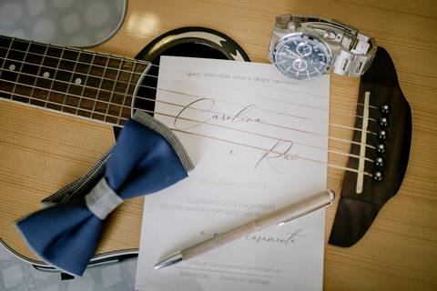 Convite de casamento personalizado, elegante e sofisticado, colocado sobre uma viola, um laço azul, relógio prateado e caneta dourada. convites de casamento únicos, acessórios elegantes e decoração'