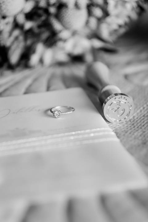 Fotografia em preto e branco de um anel de noivado elegante sobre convites de casamento personalizados com lacre artesanal. Detalhes capturados por fotógrafo de casamentos em Portugal. anel de noivado, fotógrafo de casamentos Portugal'