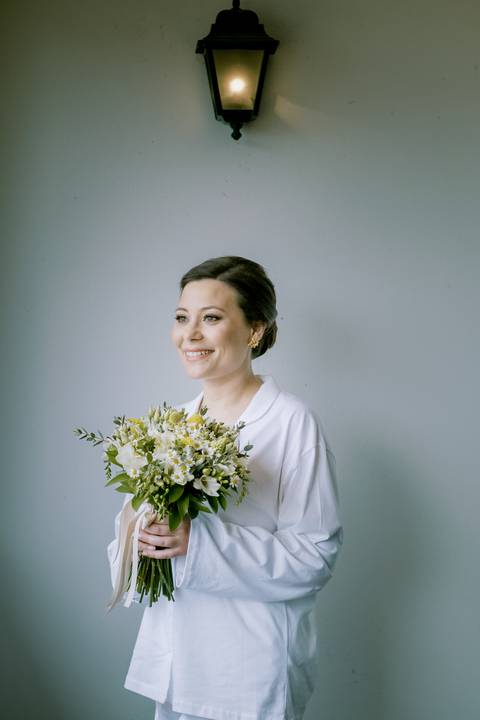 Noiva sorridente segura um bouquet de flores campestres, captada num momento de serenidade antes do casamento. Fotografia com luz suave, destacando detalhes naturais e emoções autênticas. bouquet, fotografia de casamento, retrato de noiva.'