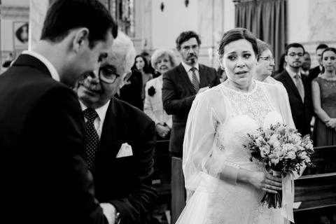 Momento emocionante durante a cerimónia de casamento: a noiva, segurando um delicado bouquet, expressa emoção enquanto o pai entrega a sua mão ao noivo. Convidados atentos ao fundo. asamento, noiva, bouquet, cerimónia, emoções, fotografia profissional.'