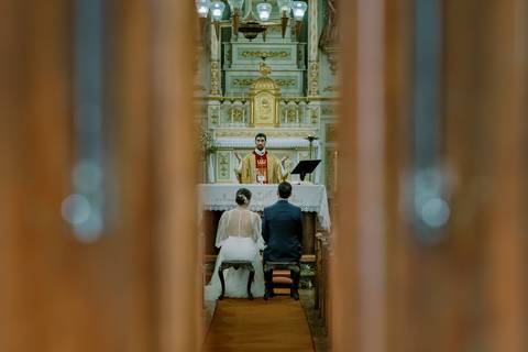 Imagem de casamento em igreja católica, com noivos ajoelhados perante o altar, padre a realizar a cerimónia. Perfeita para transmitir o significado e a beleza de um casamento religioso em Portugal. casamento, igreja'