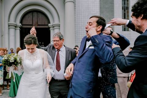Momento divertido à saída da igreja, com os noivos a serem surpreendidos por amigos e familiares. Captura natural e espontânea que reflete a felicidade do casamento. fotografia de casamento, momentos espontâneos, saída da igreja, noivos'