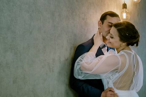 Momento íntimo de casamento, com noivos apaixonados em abraço terno junto a uma parede A noiva em vestido de renda e o noivo em fato elegante transmitem amor e cumplicidade.  fotografia de casamento, noivos, momento romântico'