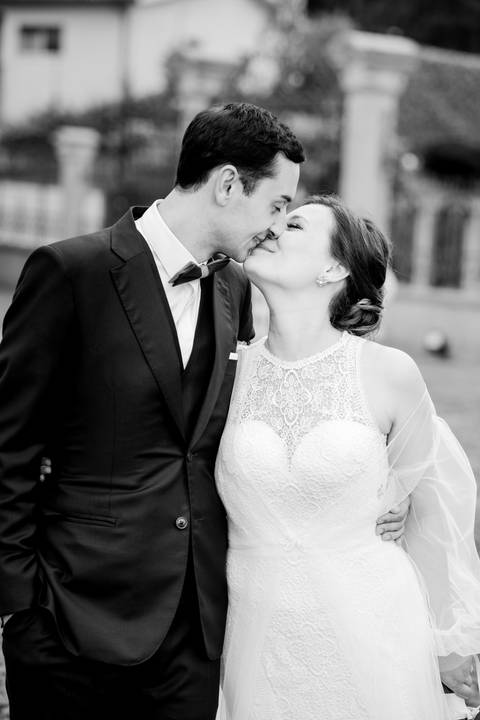 Momento romântico entre os noivos, capturado com naturalidade e emoção. A noiva com vestido rendado e o noivo de fato azul partilham um beijo apaixonado num cenário elegante. fotografia de casamento, fotógrafo em Portugal, oliveira de azeméis'
