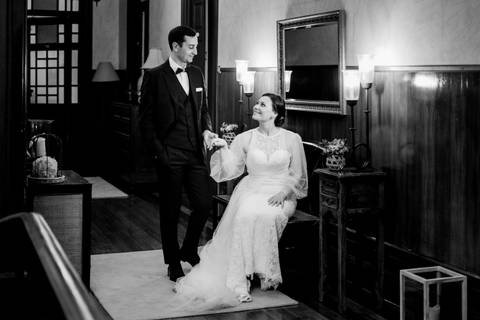 Retrato elegante e intemporal dos noivos em preto e branco, capturado num ambiente clássico e acolhedor. Destaque para a cumplicidade e detalhes do vestido de noiva e fato do noivo. fotografia de casamento, retrato de noivos, fotógrafo em portugal,'