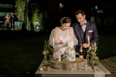 Os noivos partilham um momento especial ao cortar o bolo de casamento decorado com flores naturais, num ambiente elegante e iluminado por velas: fotógrafo de casamento, bolo de casamento, quinta de Santiago, corte do bolo, casar em portugal, '