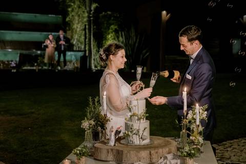Os noivos brindam ao amor com taças de champanhe junto ao bolo de casamento decorado com flores, num ambiente elegante e iluminado por velas: fotógrafo de casamento, brinde de casamento, fotografia de casamento, rui costa freire phototography.'