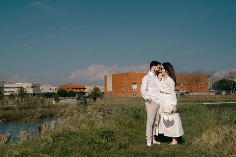 Sessão fotográfica de casal em ambiente natural junto à água, com luz natural e cenário urbano ao fundo. Momento romântico ideal para pré-casamento ou engagement. Palavras-chave: casal, amor, sessão fotográfica, pré-casamento, natureza'