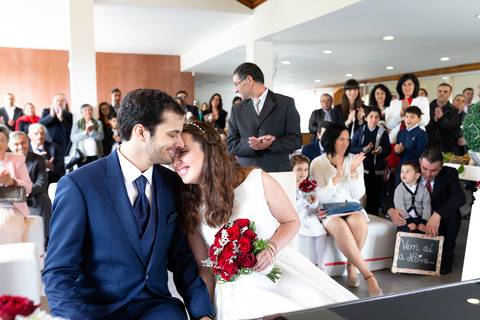 Casal apaixonado em frente a convidados, noivo de fato azul e noiva de vestido branco com bouquet de rosas vermelhas.  portfólio de fotografia de casamento, fotografia de casamento, fotógrafo de casamentos, quinta das janelas, fotógrafo cantanhede'
