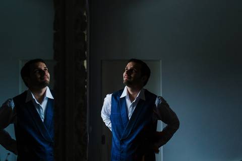 Noivo vestido com colete azul e camisa branca refletido num espelho. Fotografia elegante, sites de fotografia de casamento, preparação do noivo, fotógrafo de casamentos, casamento em Portugal, quinta das Janelas,'