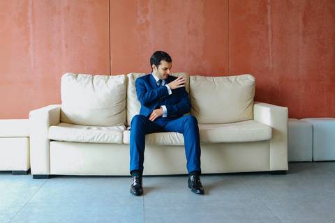 Noivo sentado num sofá branco, vestido com fato azul, fotografia de casamento, retrato de noivo e sessões fotográficas, noivo, retrato de noivo, sessão fotográfica, fotógrafo de casamentos, casamento em Coimbra.'