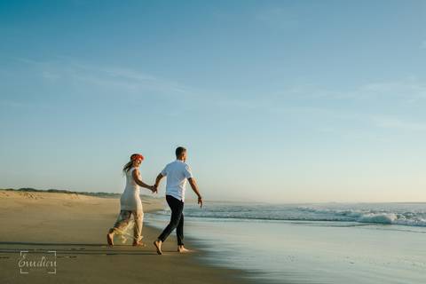 Casal a caminhar descalço junto ao mar, numa praia ao pôr do sol, com céu azul e luz dourada. Sessão fotográfica de casamento em ambiente natural, captando momentos de amor e cumplicidade. Fotografia profissional, perfeita para casamentos na praia.'