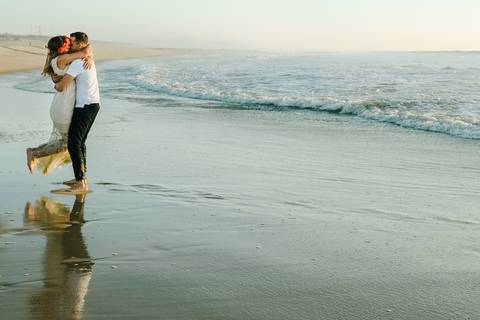 Casal abraça-se apaixonadamente na praia, com o reflexo na água e o mar como pano de fundo, num momento romântico ao pôr do sol. fotógrafo de casamento, sessão na praia, momentos espontâneos, praia da tocha Cantanhede, rui costa freire Photography'