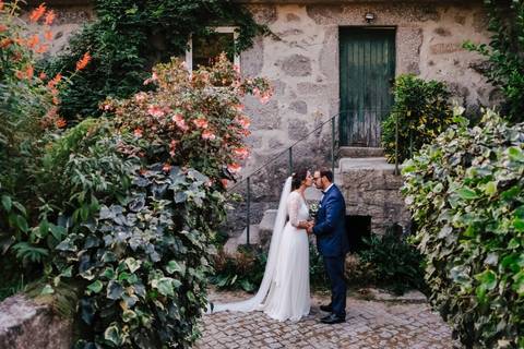 noivos beijam-se junto a casa de pedra na quinta da torre rodeados por flores'