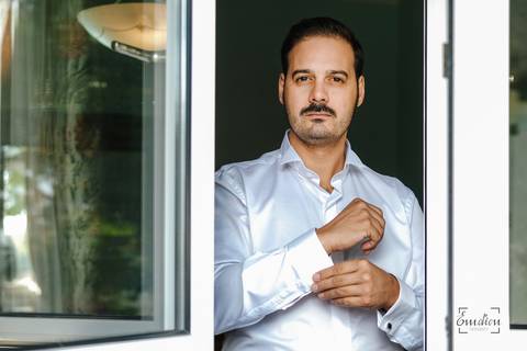 noivo prepara-se à janela e aperta botão do punho da camisa'