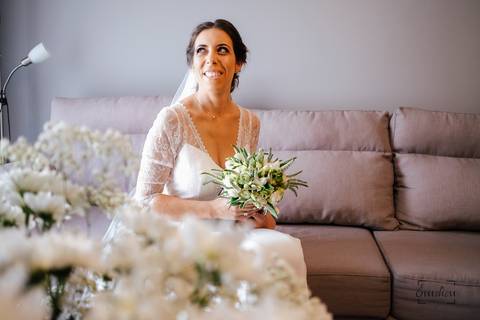 noiva sentada no sofá da sala segurando o bouquet e a sorrir'