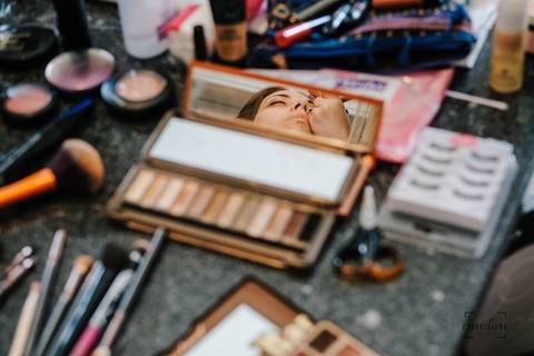 noiva espelhada na paleta de maquilhagem enquanto está a ser maquilhada'