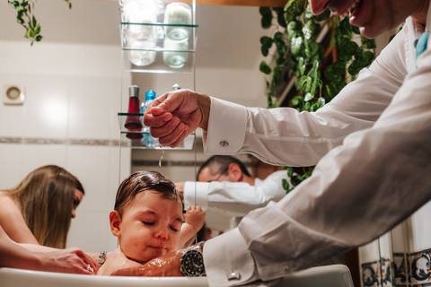 padrinho dá banho à criança no dia do baptizado'