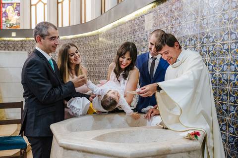 padre coloca água na cabeça da criança no momento do baptismo'