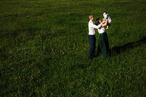 pais brincam com a criança no parque verde da cidade de coimbra no dia do baptizado'